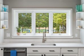 Une cuisine dotée d’un évier à deux bacs, de meubles blancs et d’une fenêtre donnant sur un paysage verdoyant.