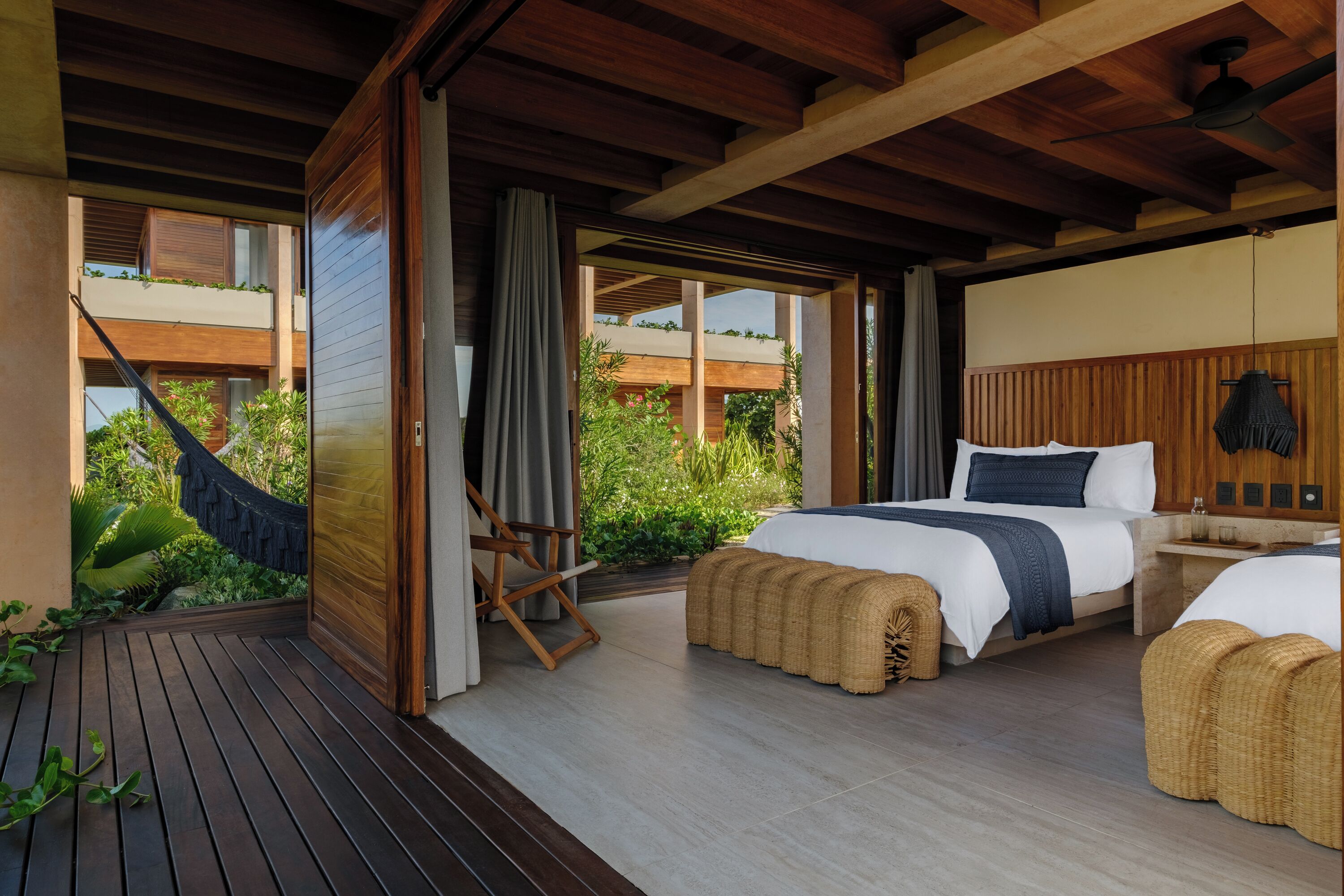 A modern bedroom with a large bed, a wooden ceiling, and a view of greenery outside.