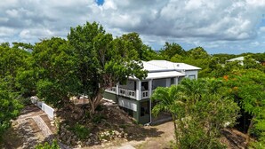 A two-story house with a balcony, surrounded by lush greenery and trees. - Charming 2-bedroom Villa (Pares)