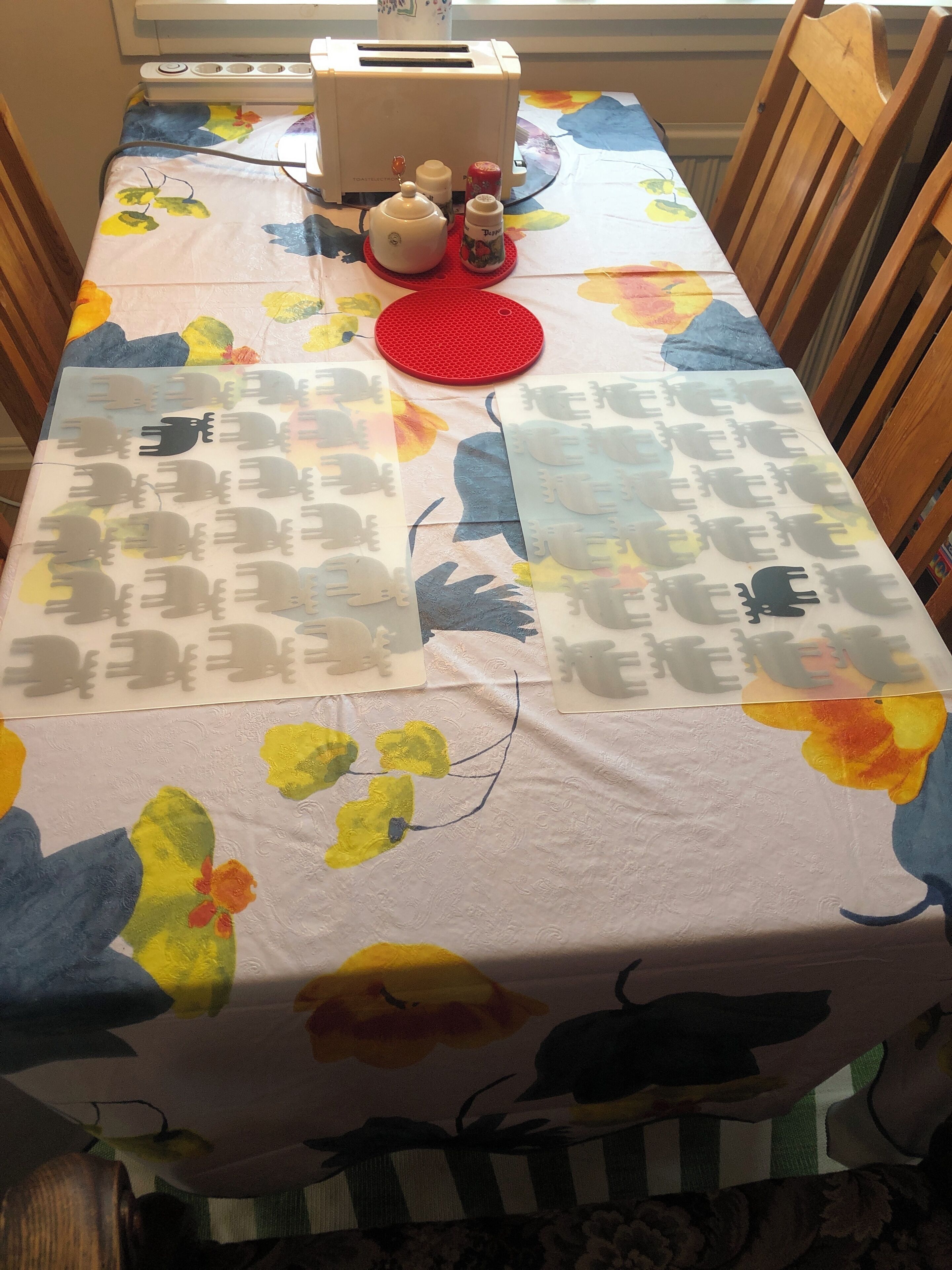 A dining table with a floral tablecloth, a toaster, a red placemat, and a bottle of syrup. - Cozy Cottage in Stockholms Archipelago (Stockholms län)