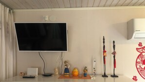 A room with a flat-screen TV mounted on the wall, a white air conditioning unit, a white cabinet with drawers, and a small statue on the counter. - Cozy Cottage in Stockholms Archipelago (Stockholms län)
