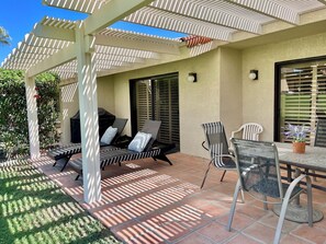 Zona patio con posti a sedere all'aperto, tra cui un tavolo e sedie, sotto una struttura a pergola.