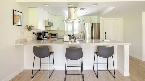 Una cocina moderna con una isla grande, taburetes de bar y electrodomésticos de acero inoxidable.