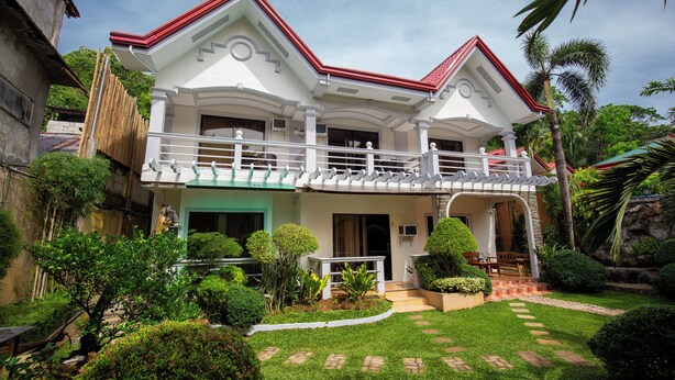 A two-story house with a balcony, surrounded by well-maintained gardens and palm trees. - Vilus Place  (Boracay Island)