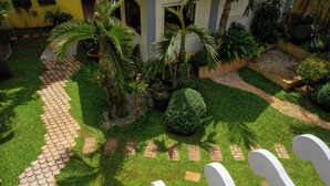 A well-maintained garden with a paved walkway, various plants, and a white fence. - Vilus Place  (Boracay Island)