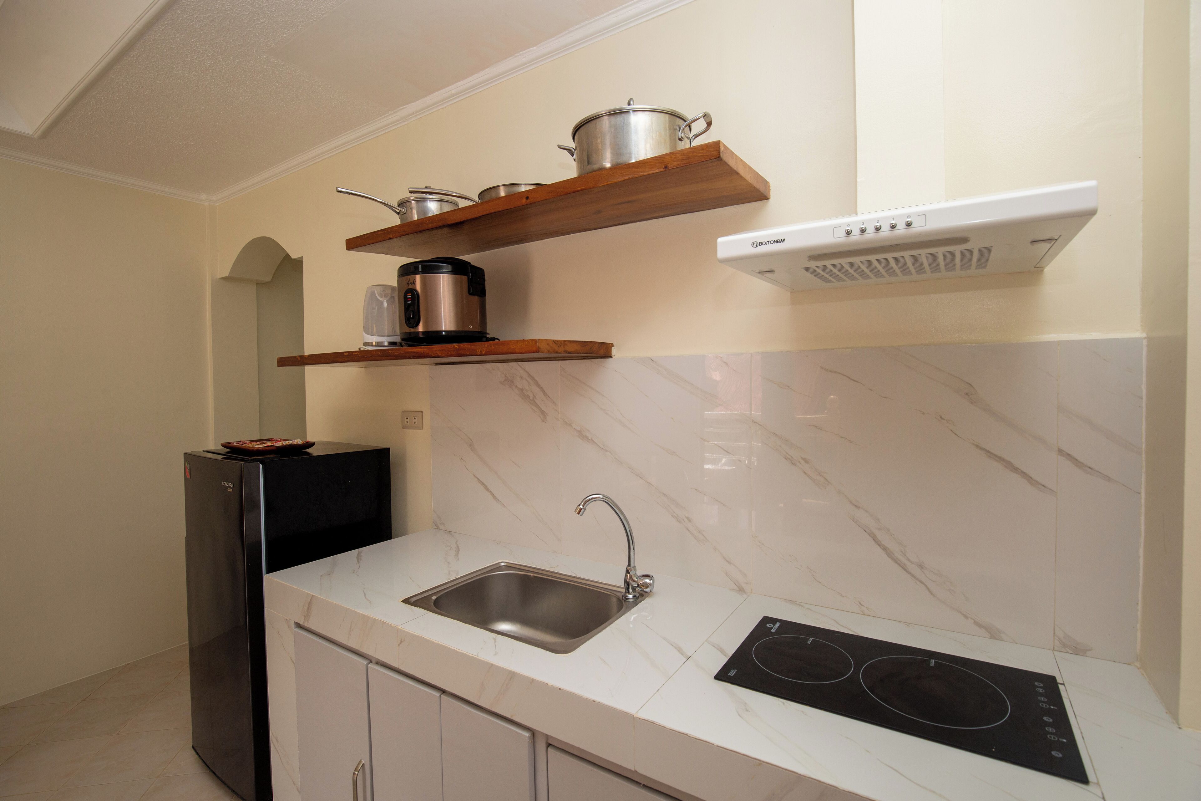 Una cocina con un lavamanos de acero inoxidable, una estufa empotrada, un microondas y repisas de madera sobre la estufa.