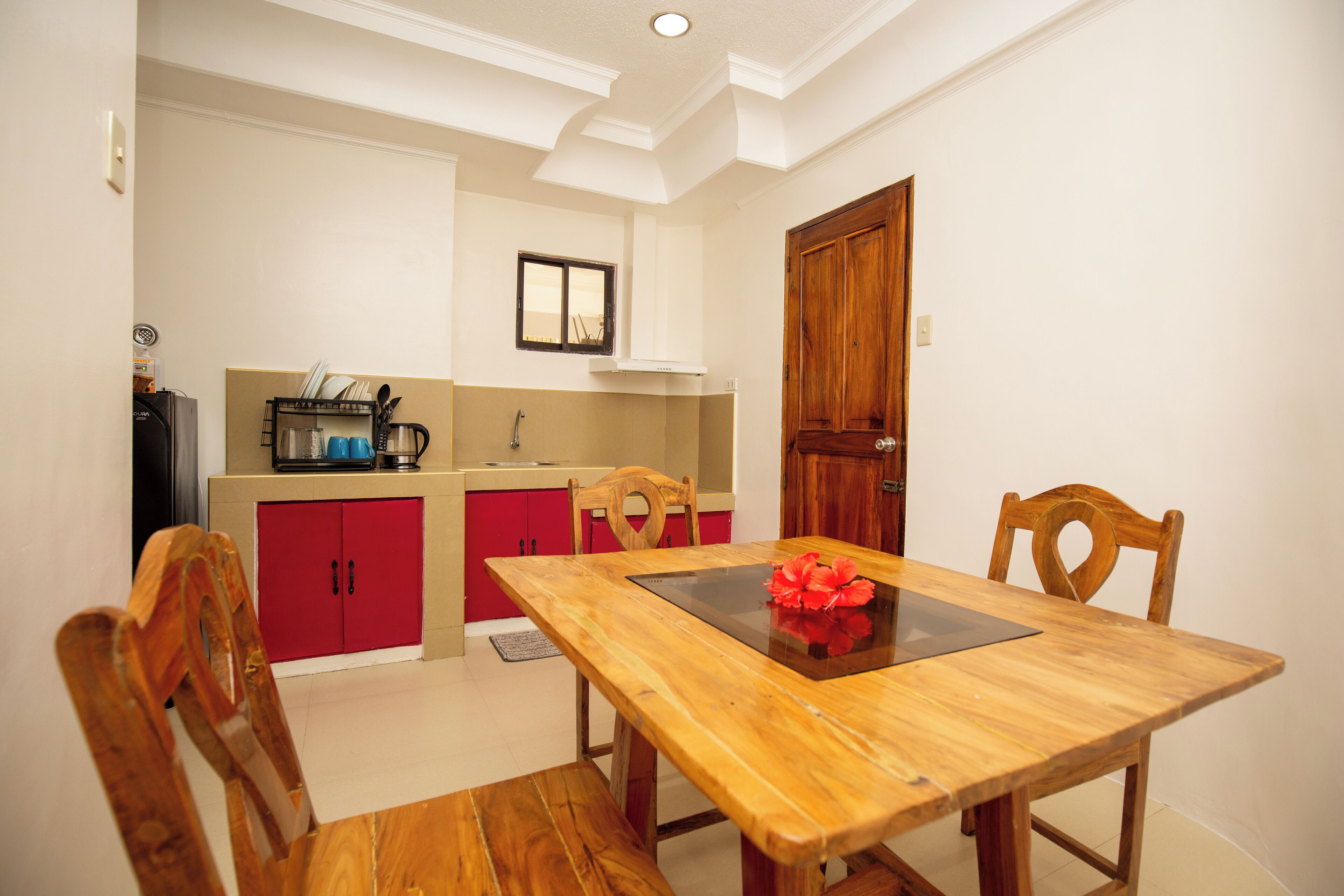 Un coin repas avec une table et des chaises en bois, un buffet rouge et, au fond, une cuisine.