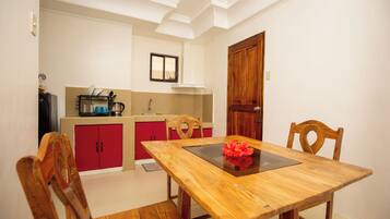 Uma sala de jantar com mesa e cadeiras de madeira, um armário vermelho e uma cozinha ao fundo.
