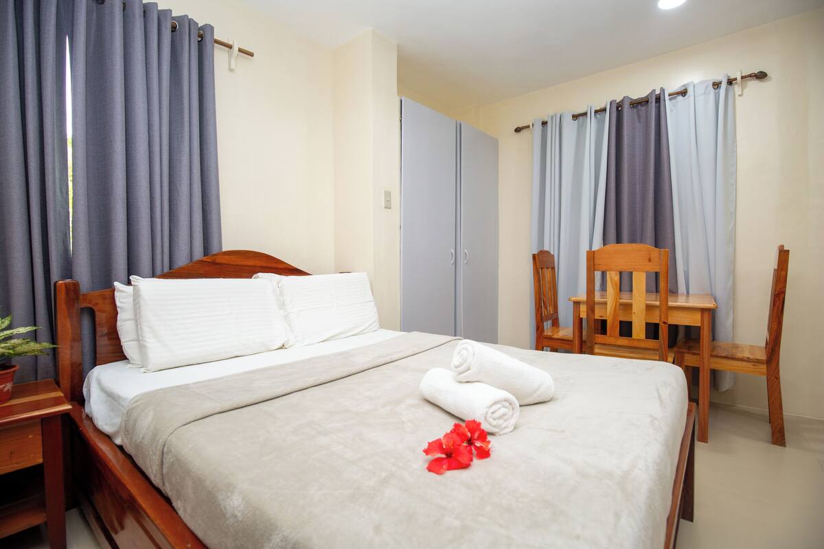A hotel room with a bed, two chairs, a wardrobe, and curtains.