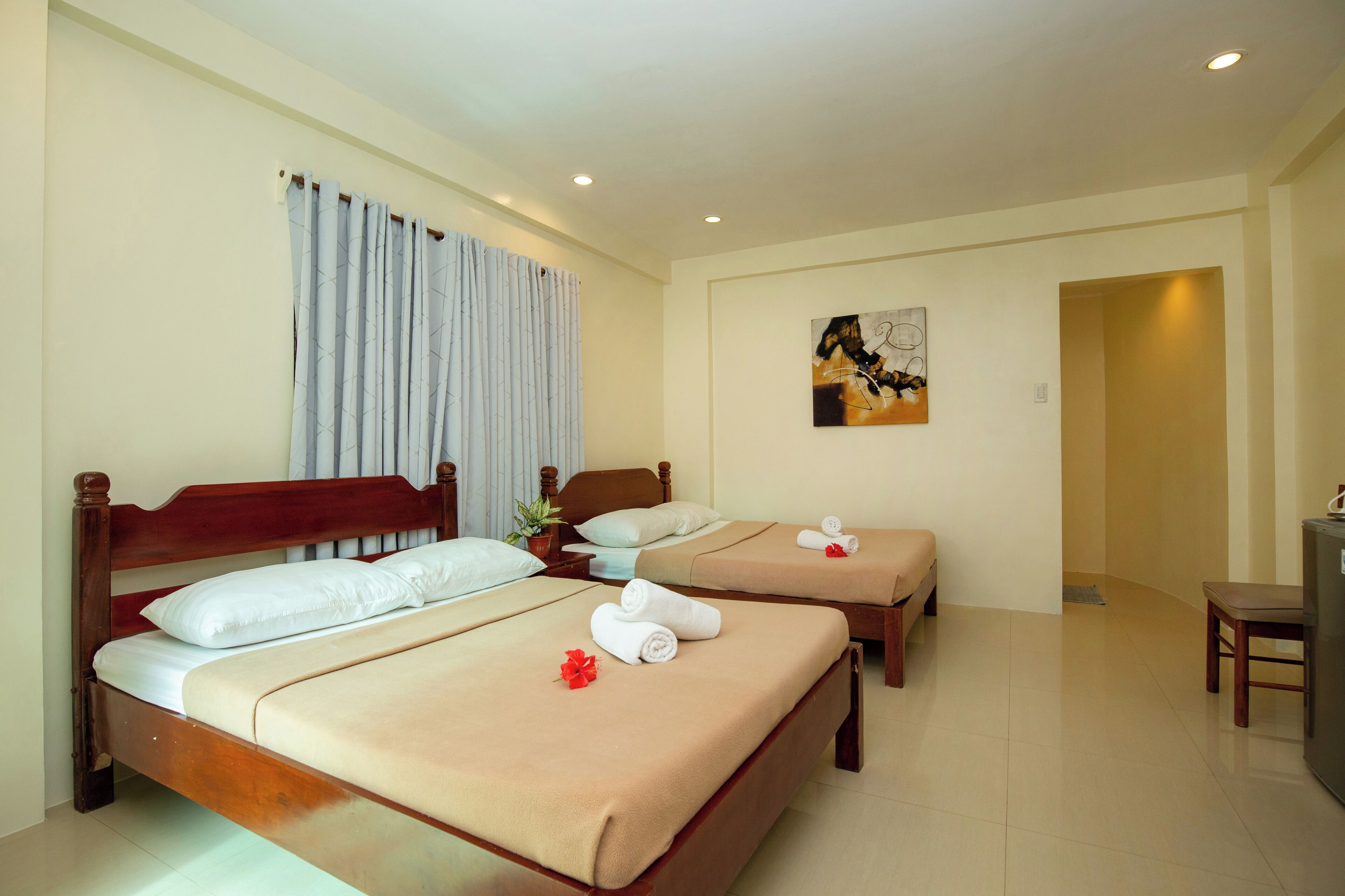 Una habitación de hotel con dos camas de madera, ropa de cama color beige y un escritorio pequeño con una silla.