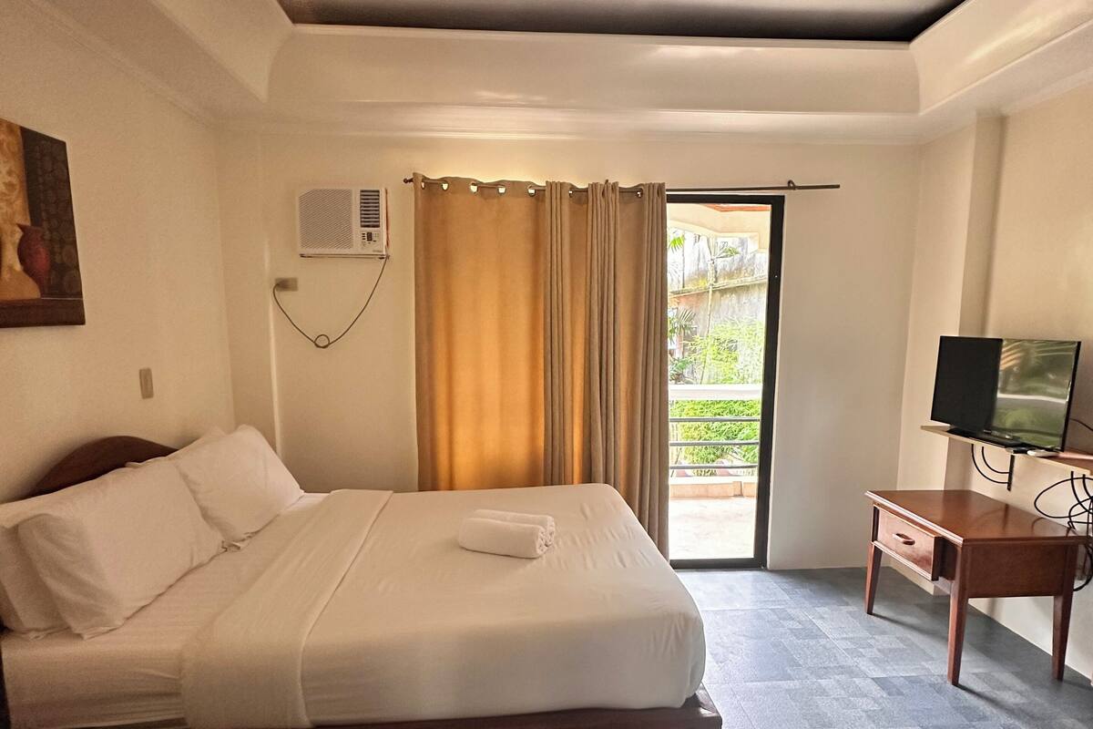 A hotel room with a bed, a desk with a TV, and a sliding glass door to the outside.