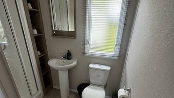 A compact bathroom with a pedestal sink, toilet, and a window with blinds.