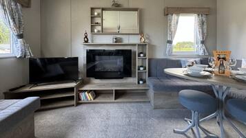 A cozy living room with a flat-screen TV, a fireplace, a sofa, a dining table with chairs, and a bookshelf.