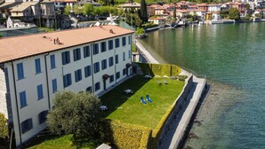 A building with a red-tiled roof, a grassy courtyard with lounge chairs, and a waterfront view. - Nice apartment for 4 people with WIFI, TV and patio (Musso)