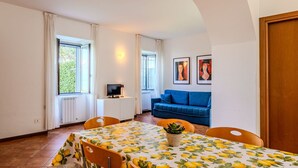 A dining area with a table covered in a lemon pattern, a blue sofa, and two framed artworks on the wall. - Lovely apartment for 4 guests with WIFI, TV and patio (Musso)