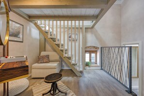 A spacious living area with a wooden staircase, a sofa, a coffee table, and a view of the upper floor.