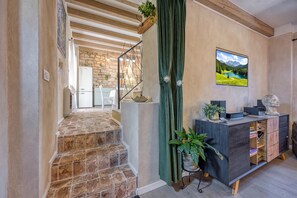 A staircase leading to a kitchen area with stone flooring, a wooden ceiling, and a green curtain.