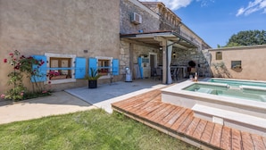 Un bâtiment en pierre doté d’une terrasse en bois, d’une piscine et d’un espace extérieur aménagé et abrité.