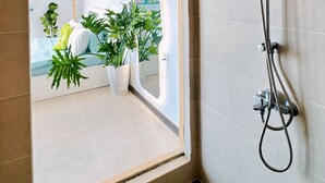 Une salle de bain moderne équipée d’une douche, d’un miroir et offrant une vue sur un espace de vie agrémenté de plantes et d’un canapé.