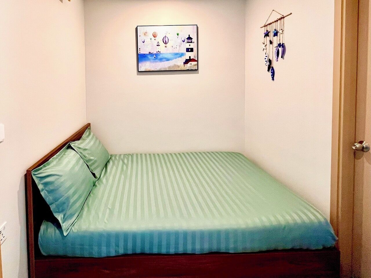 Ein kleines Zimmer mit einem Einzelbett, einer grünen Tagesdecke, einem gerahmten Bild an der Wand und einer Wandhalterung.