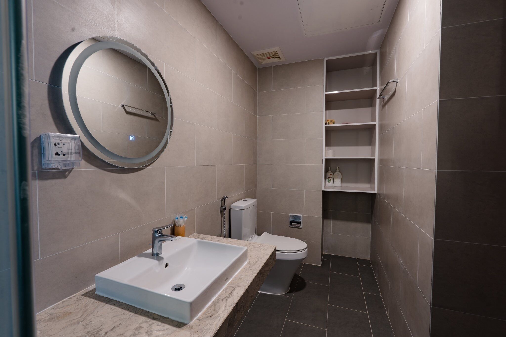 Un baño moderno con un lavamanos rectangular, un inodoro y un estante empotrado.