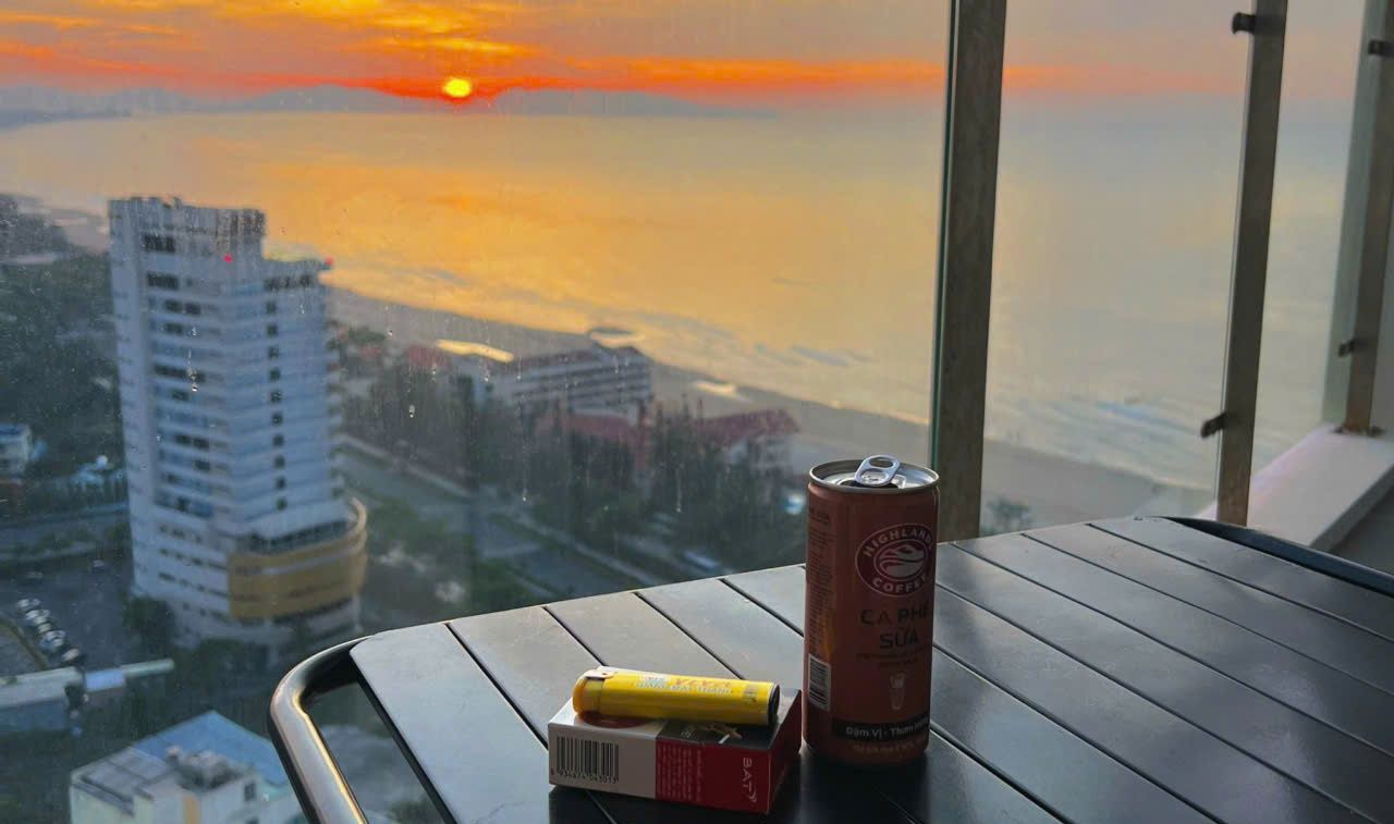 A table with a can of coffee and a yellow object, overlooking a cityscape at sunset.