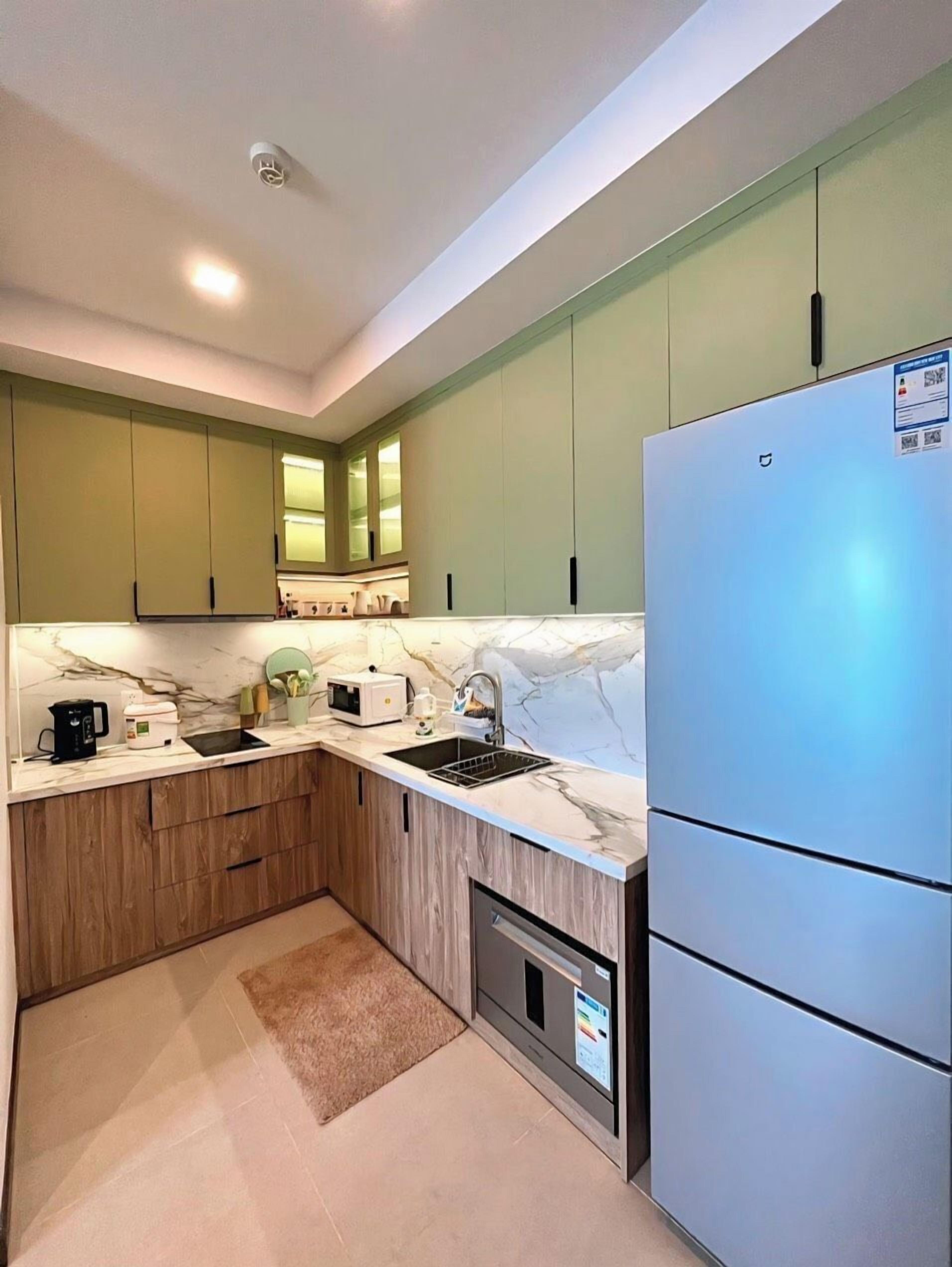 A compact kitchen with green cabinets, a white marble countertop, a stainless steel refrigerator, and a built-in oven.