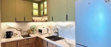 A compact kitchen with green cabinets, a white marble countertop, a stainless steel refrigerator, and a built-in oven.