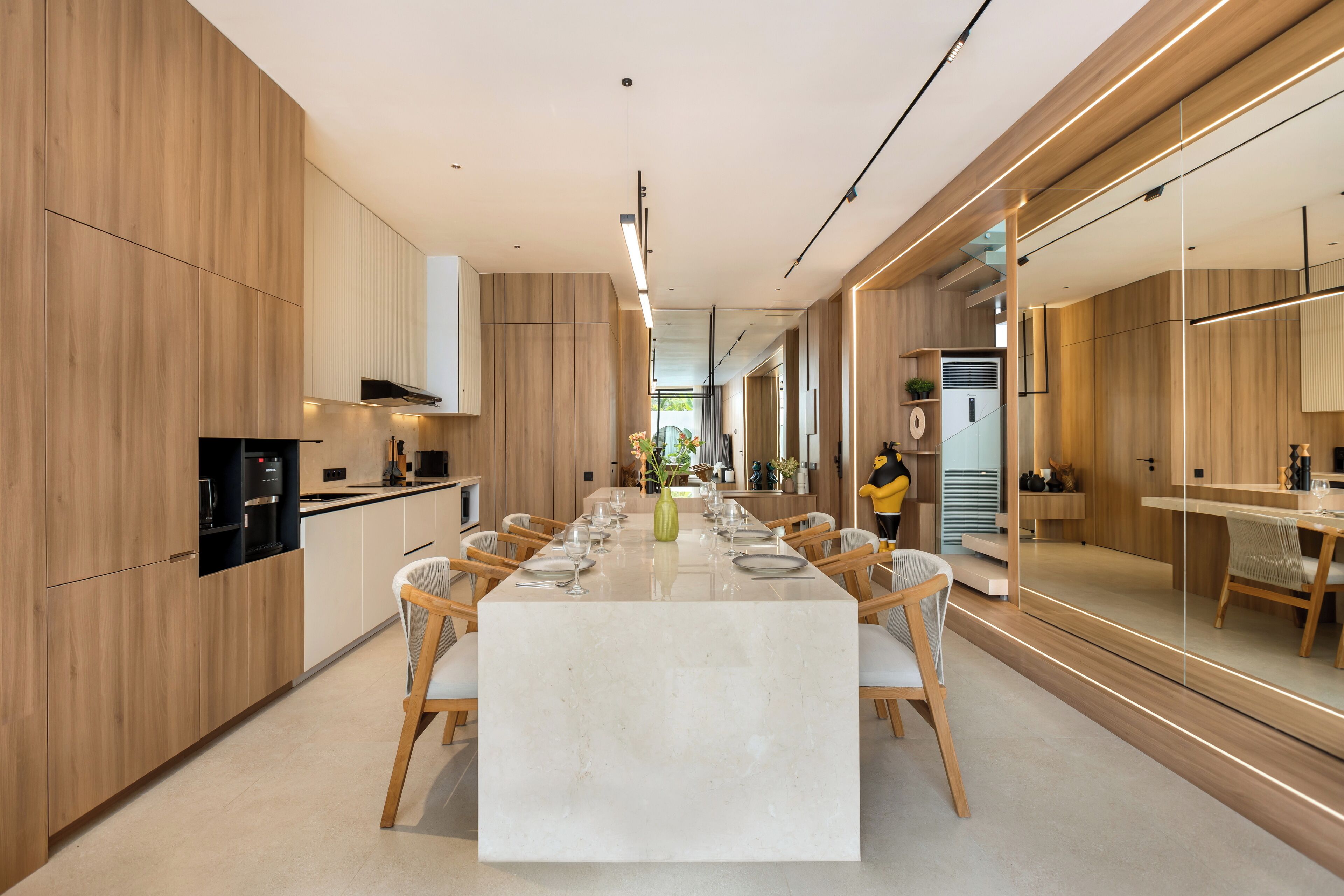 Een moderne keuken met houten kastjes, een centraal eiland met zitplaatsen, en een eethoek met een lange tafel.