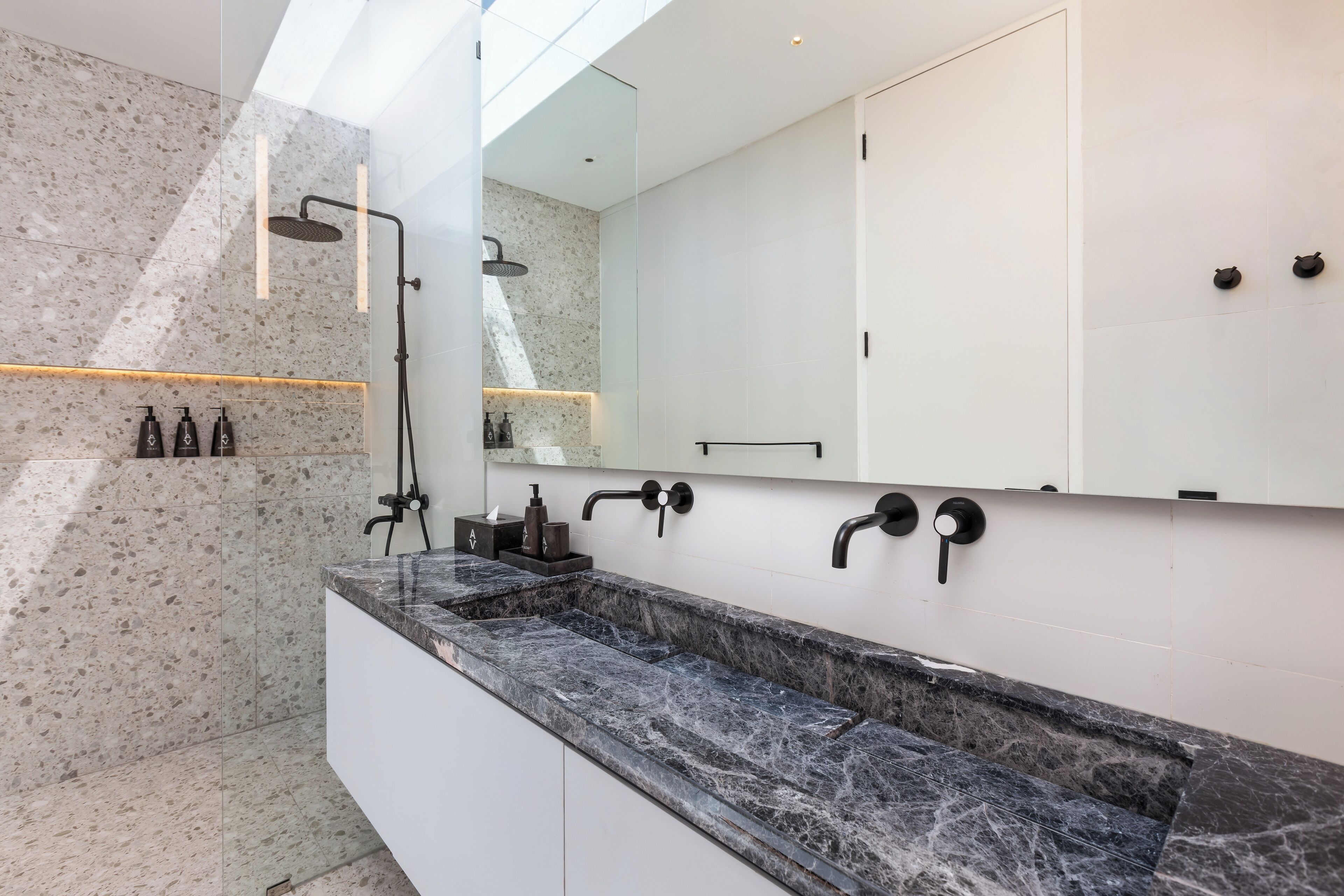 Un baño moderno con un espejo grande, una ducha con cabezal de ducha manual y un encimera de mármol.