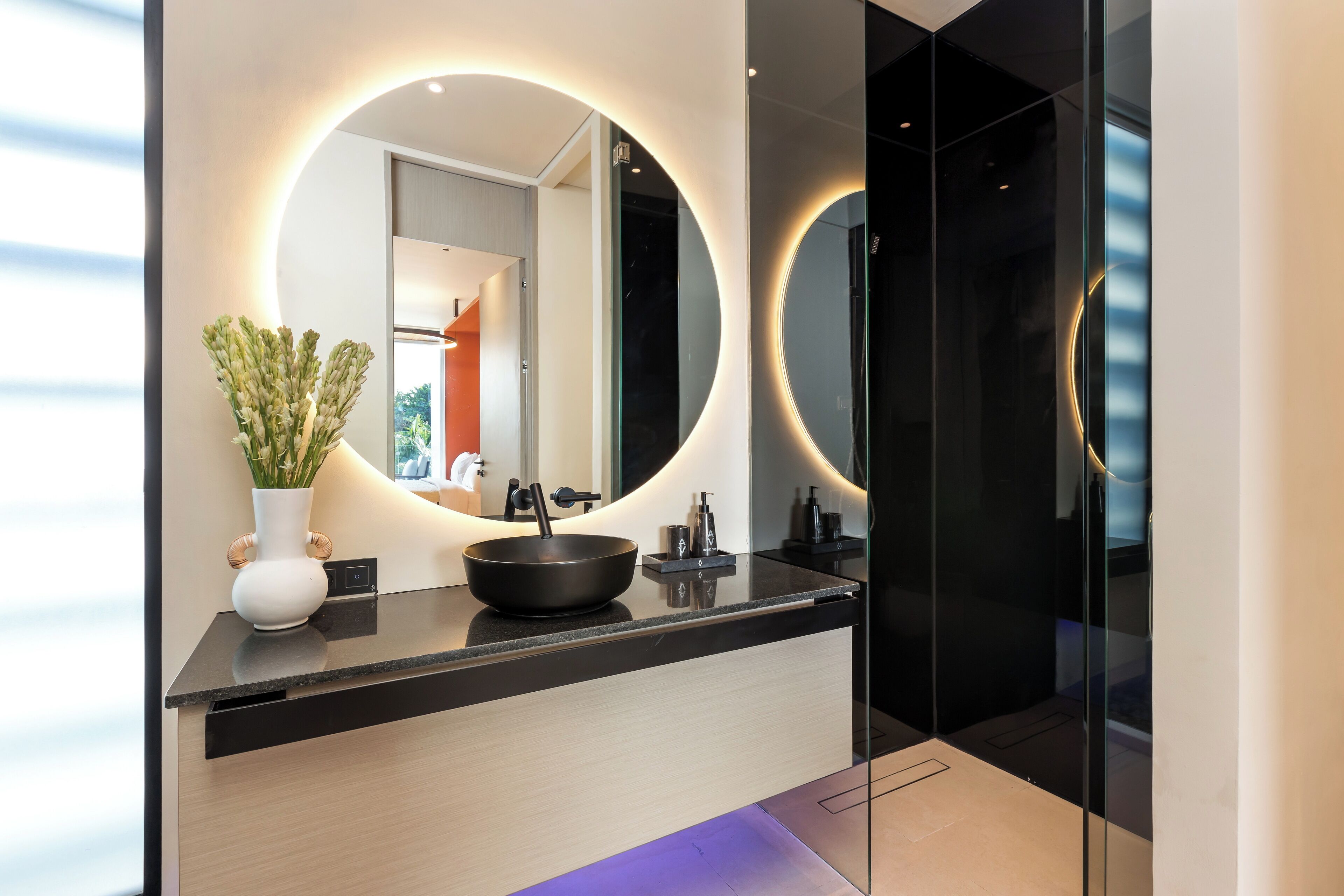 A modern bathroom with a black countertop, a round mirror, and a potted plant.