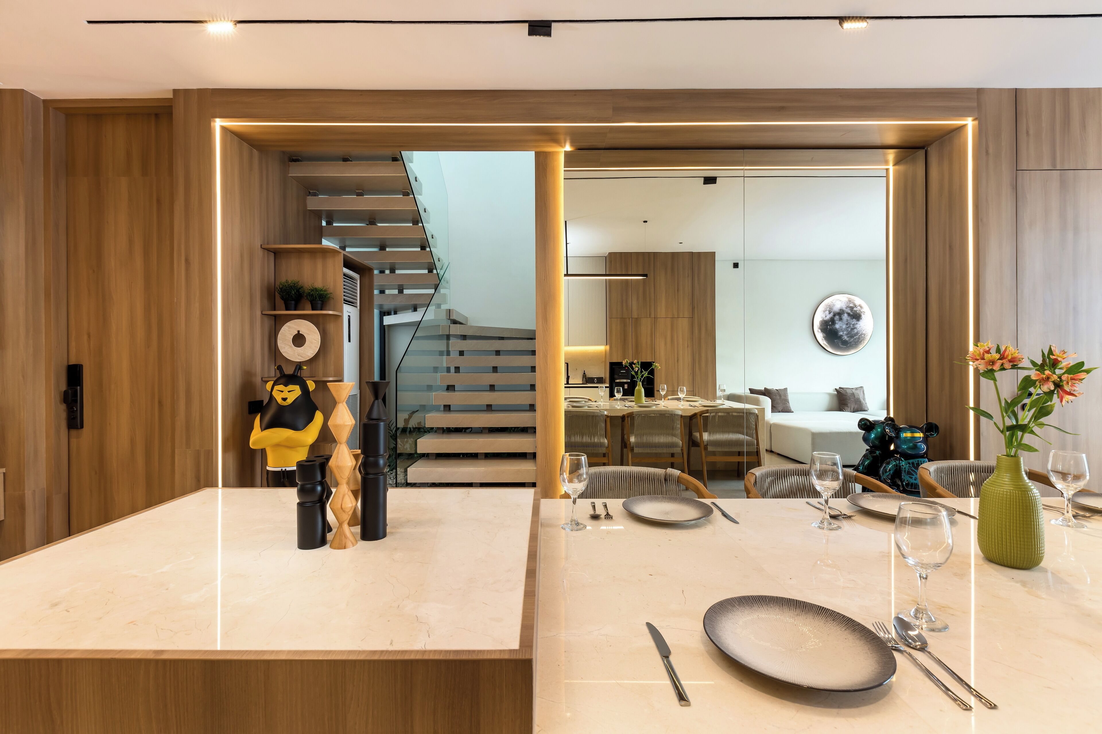 A modern dining area with a marble table, wooden accents, and a staircase leading to an upper level.