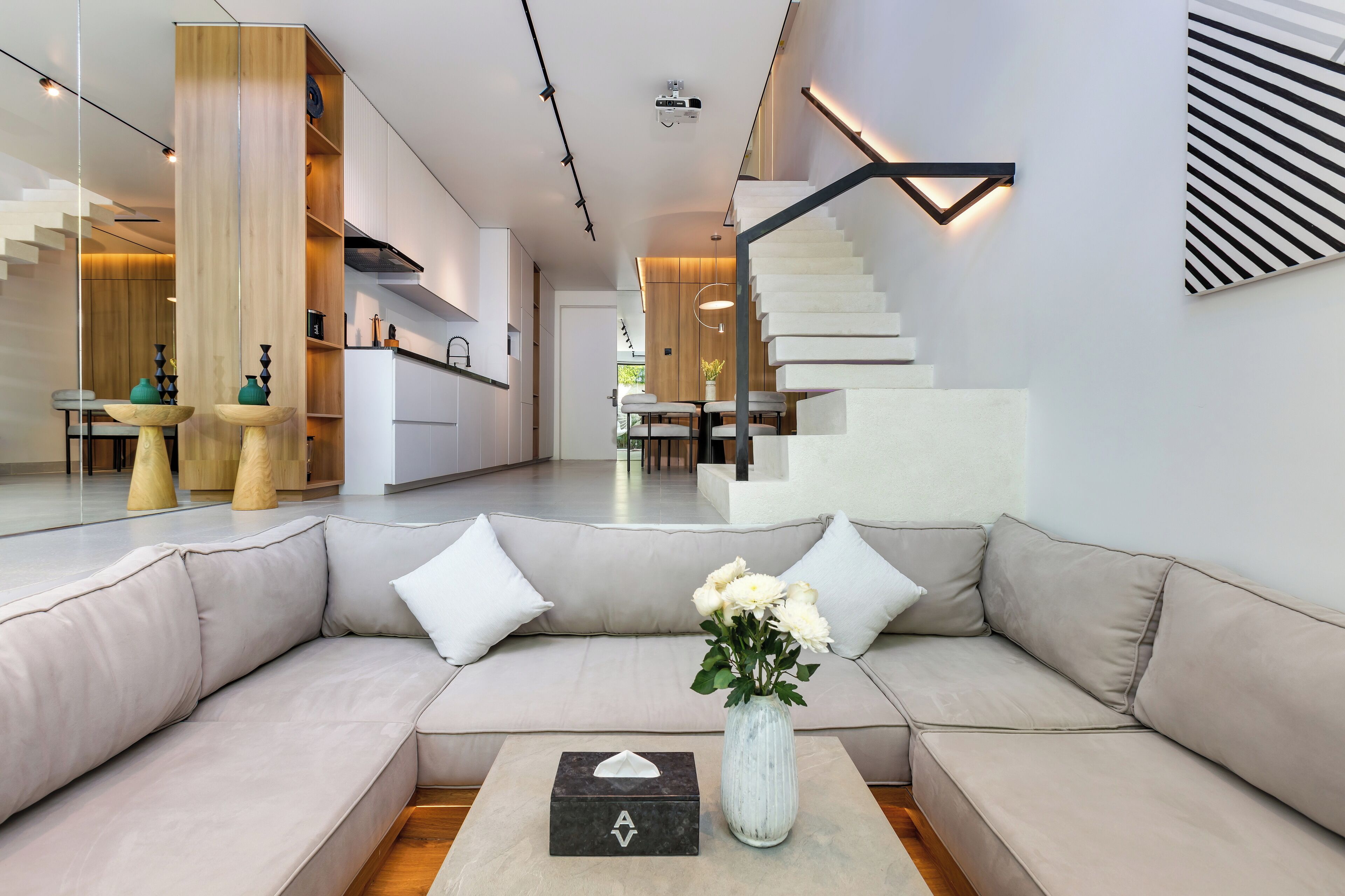 A modern living room with a beige sectional sofa, a vase with flowers, and a tissue box.