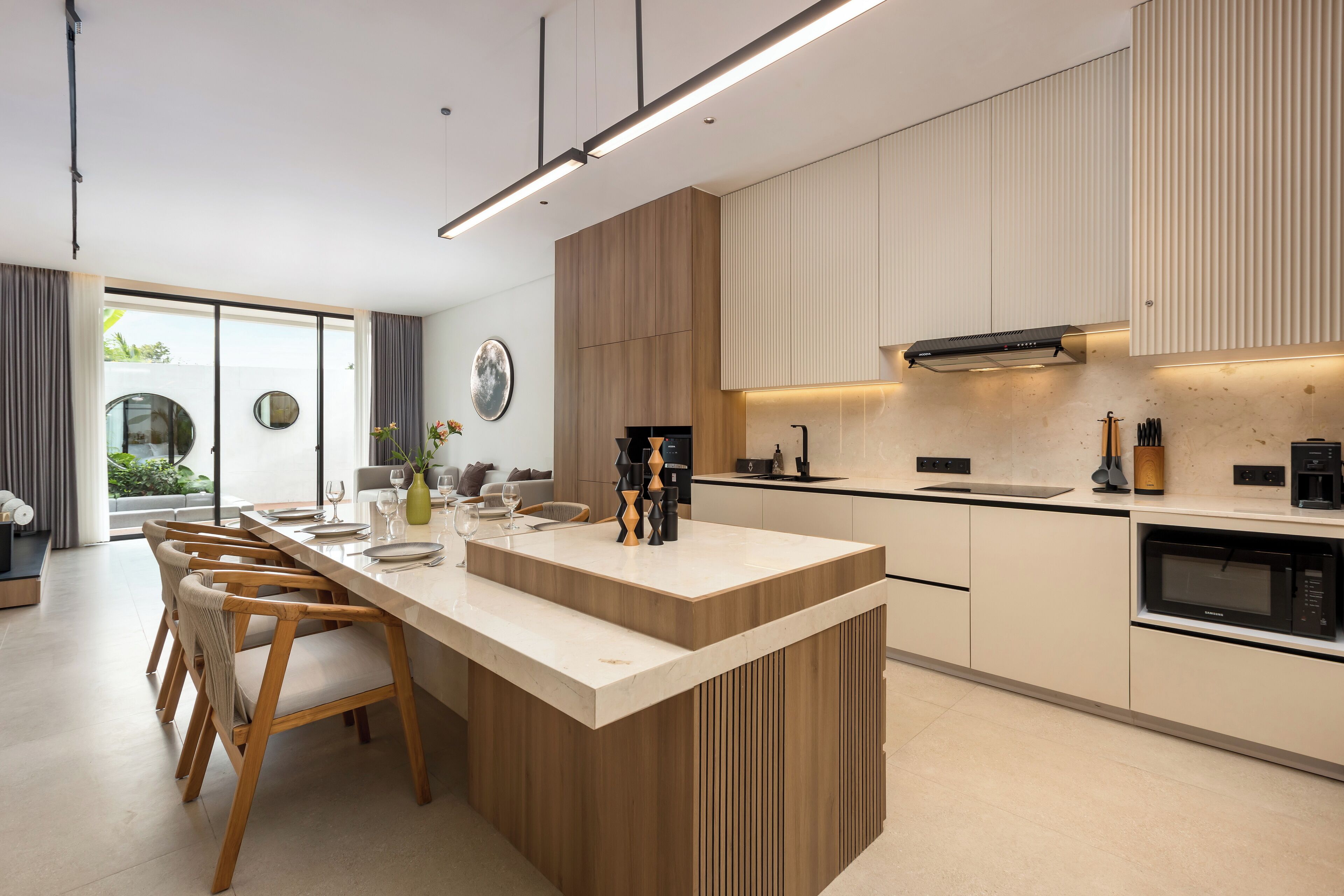 A modern kitchen with a central island, wooden chairs, and a built-in oven.