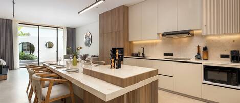 A modern kitchen with a central island, wooden chairs, and a built-in oven.