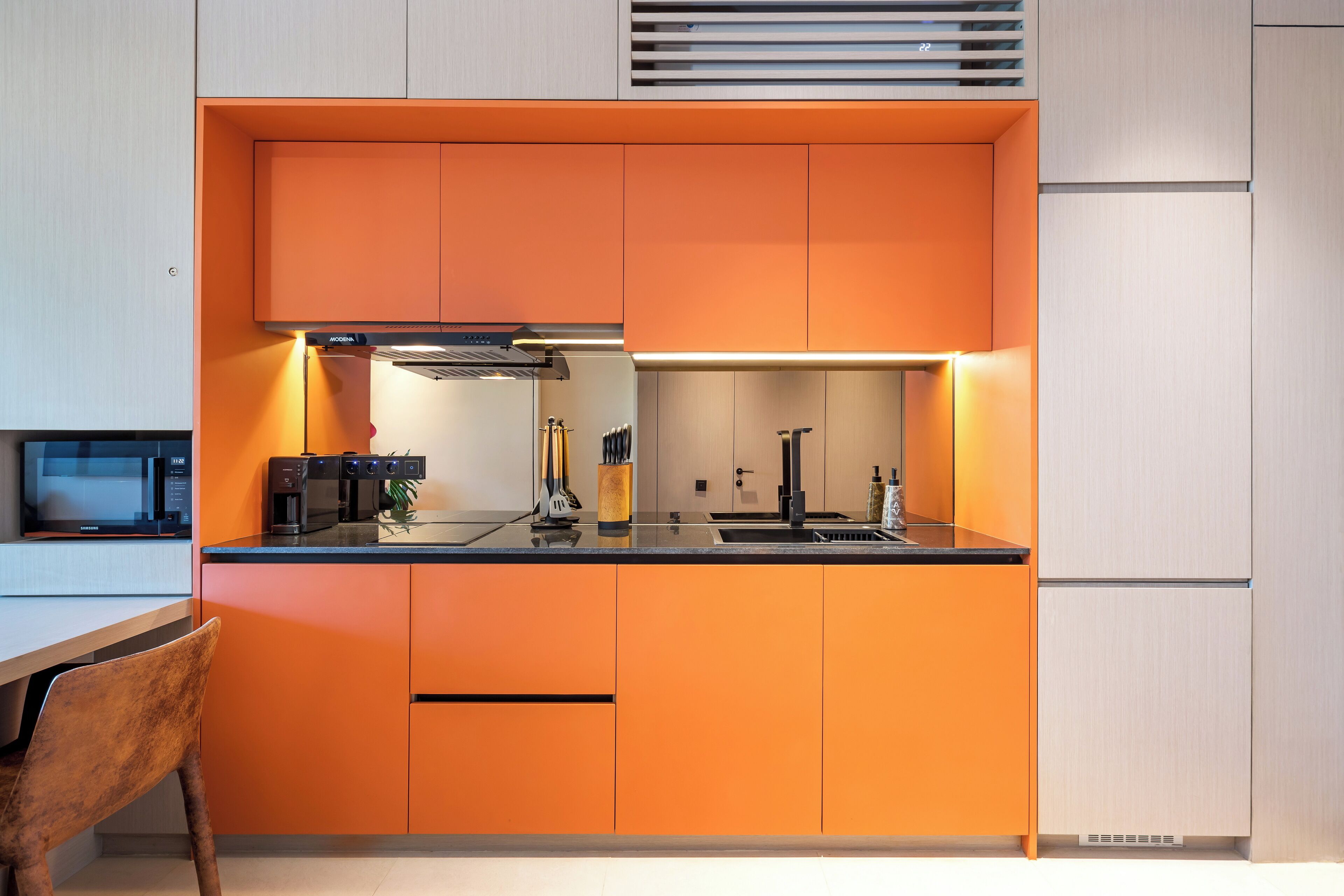 A modern kitchen with orange cabinetry, a black countertop, and stainless steel appliances.