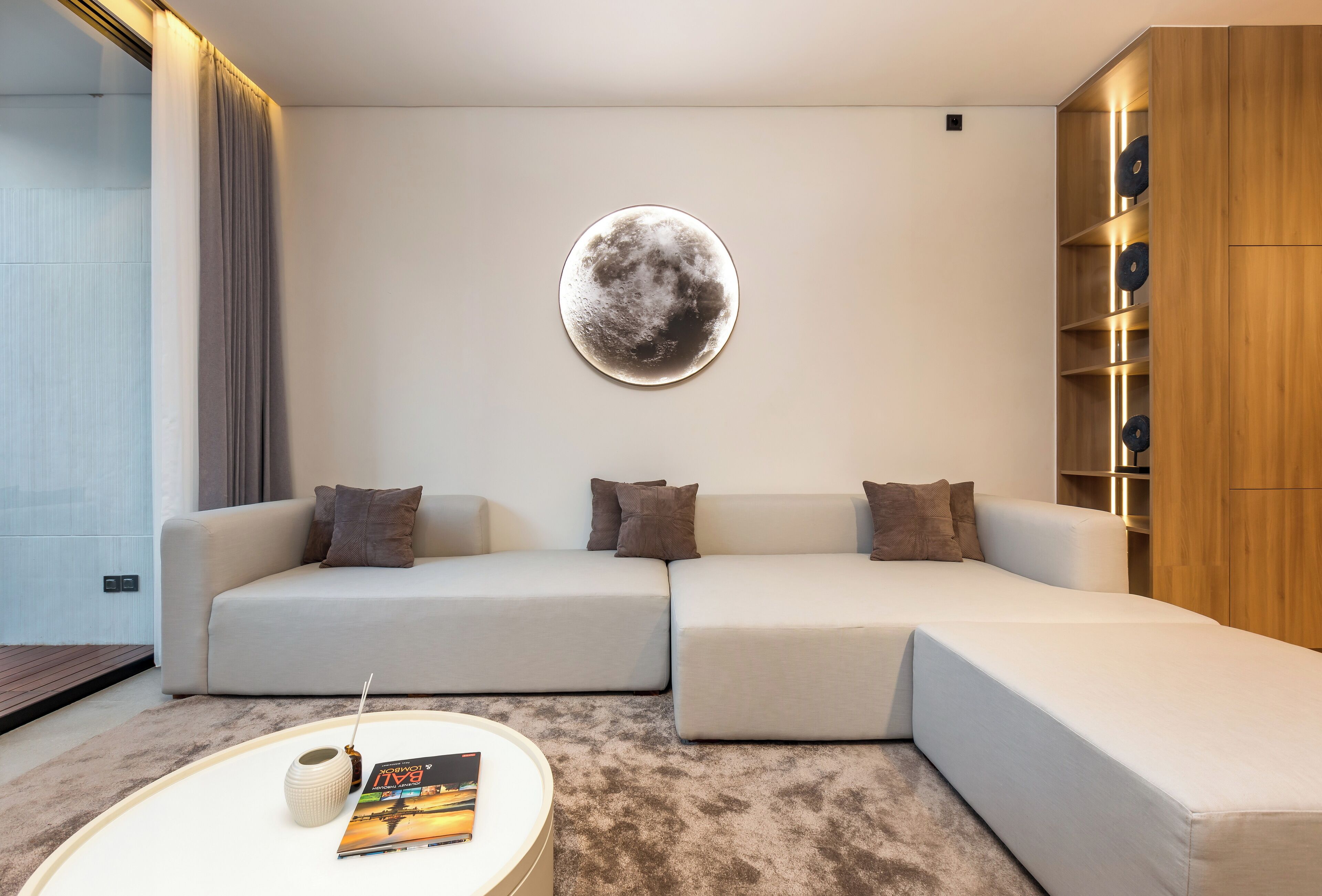 A modern living room with a sectional sofa, a round coffee table with a magazine, and a wall-mounted circular artwork.