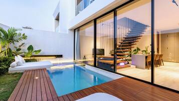 A modern house with a swimming pool, wooden deck, and a glass-enclosed living area with a staircase.