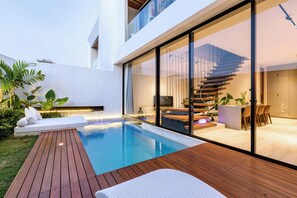 Une maison moderne dotée d’une piscine, d’une terrasse en bois et d’un salon entièrement vitré, accessible par un escalier.