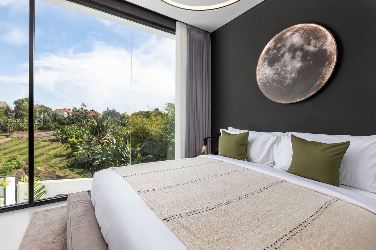 A modern bedroom with a large bed, a view of a green landscape, and a round wall decoration.