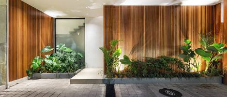 Un espacio interior moderno con un muro de listones de madera, suelo de baldosas y varias plantas.