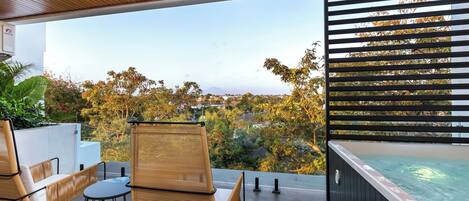 Un área de estar moderna al aire libre con un jacuzzi, con vistas a un paisaje con árboles y una montaña distante.