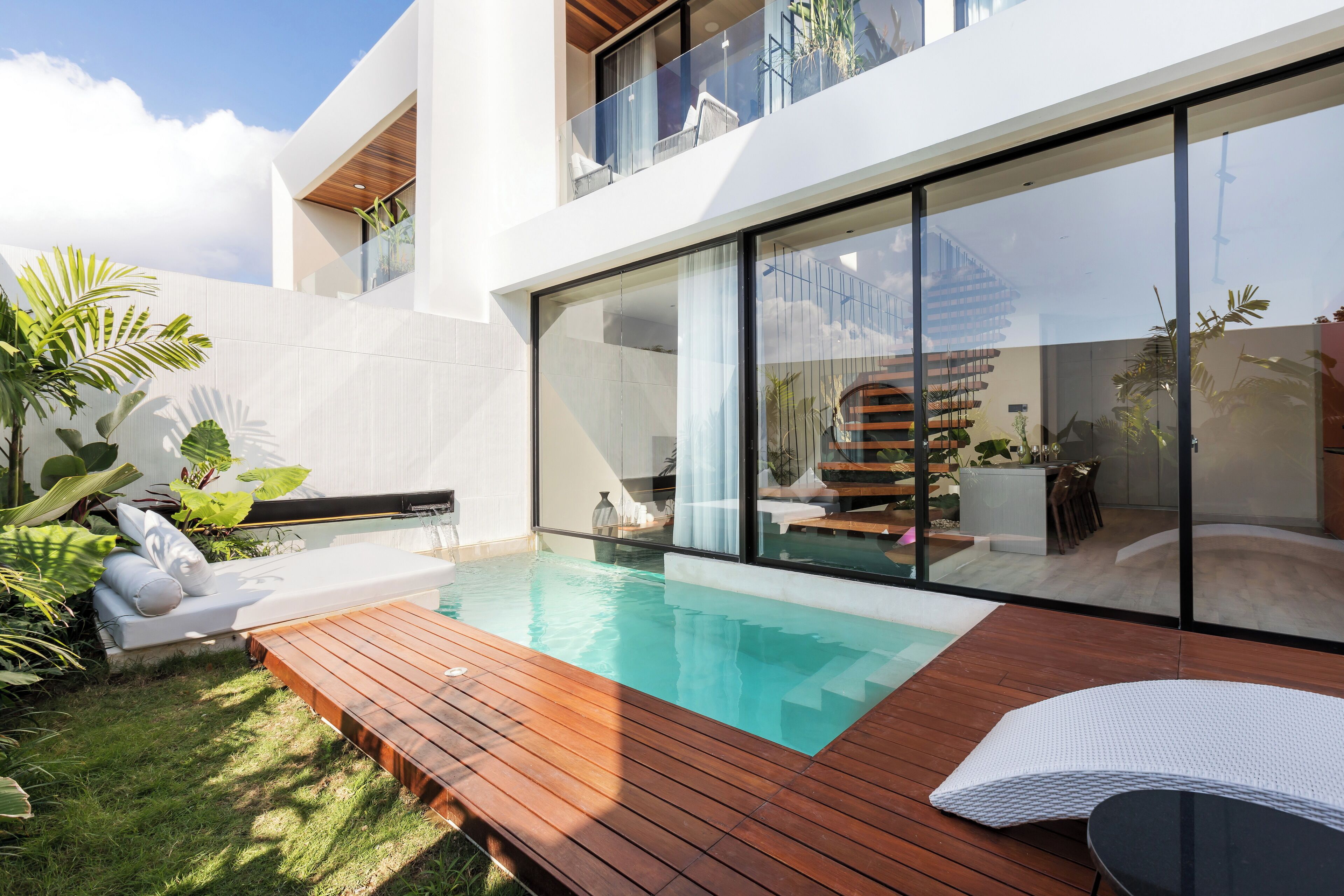Ein moderner Poolbereich im Freien mit einer Holzterrasse, einer Liege und einer patioartigen Glasveranda.