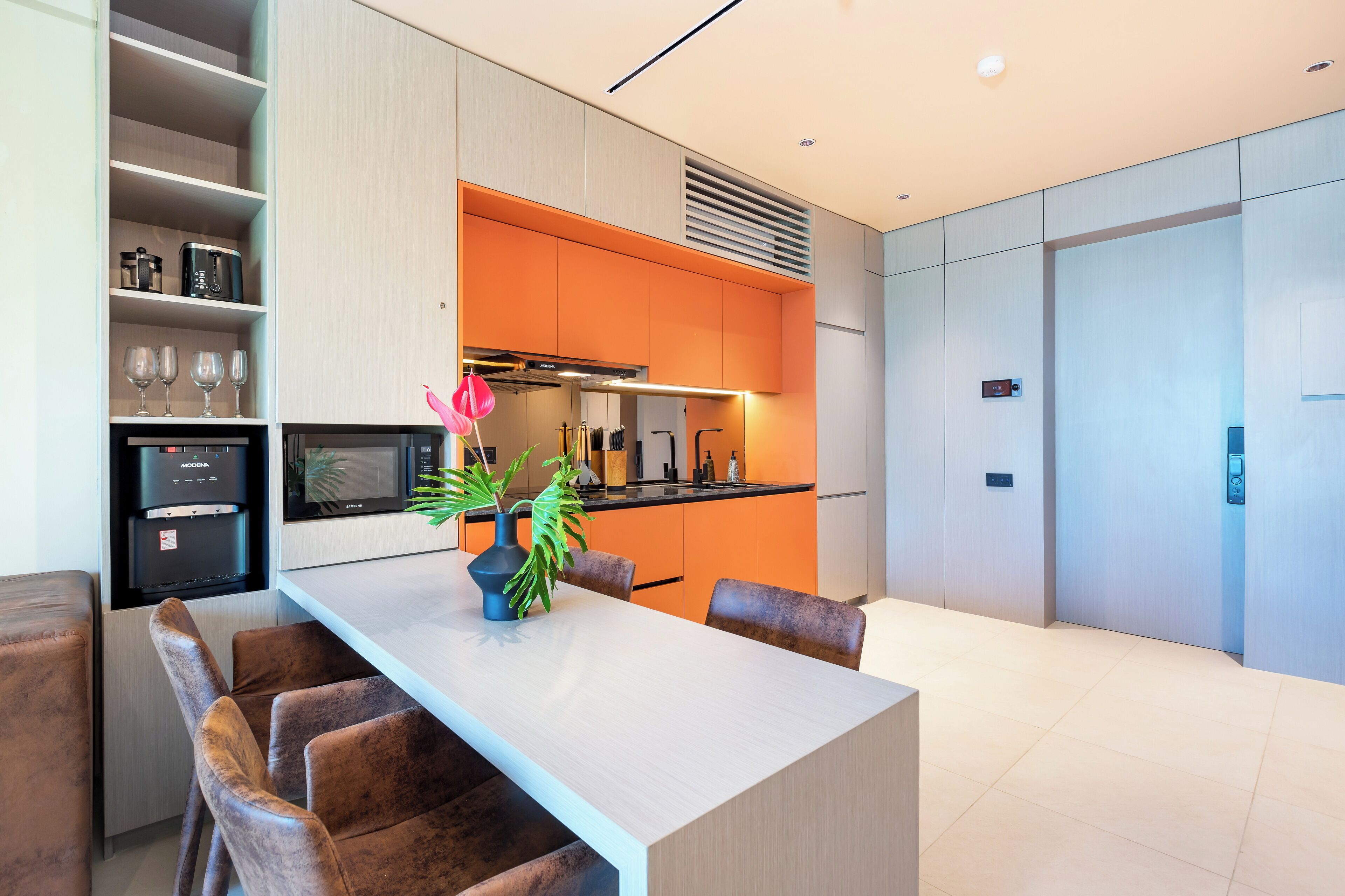 A modern kitchen with a central island, built-in appliances, and a bright orange accent wall.