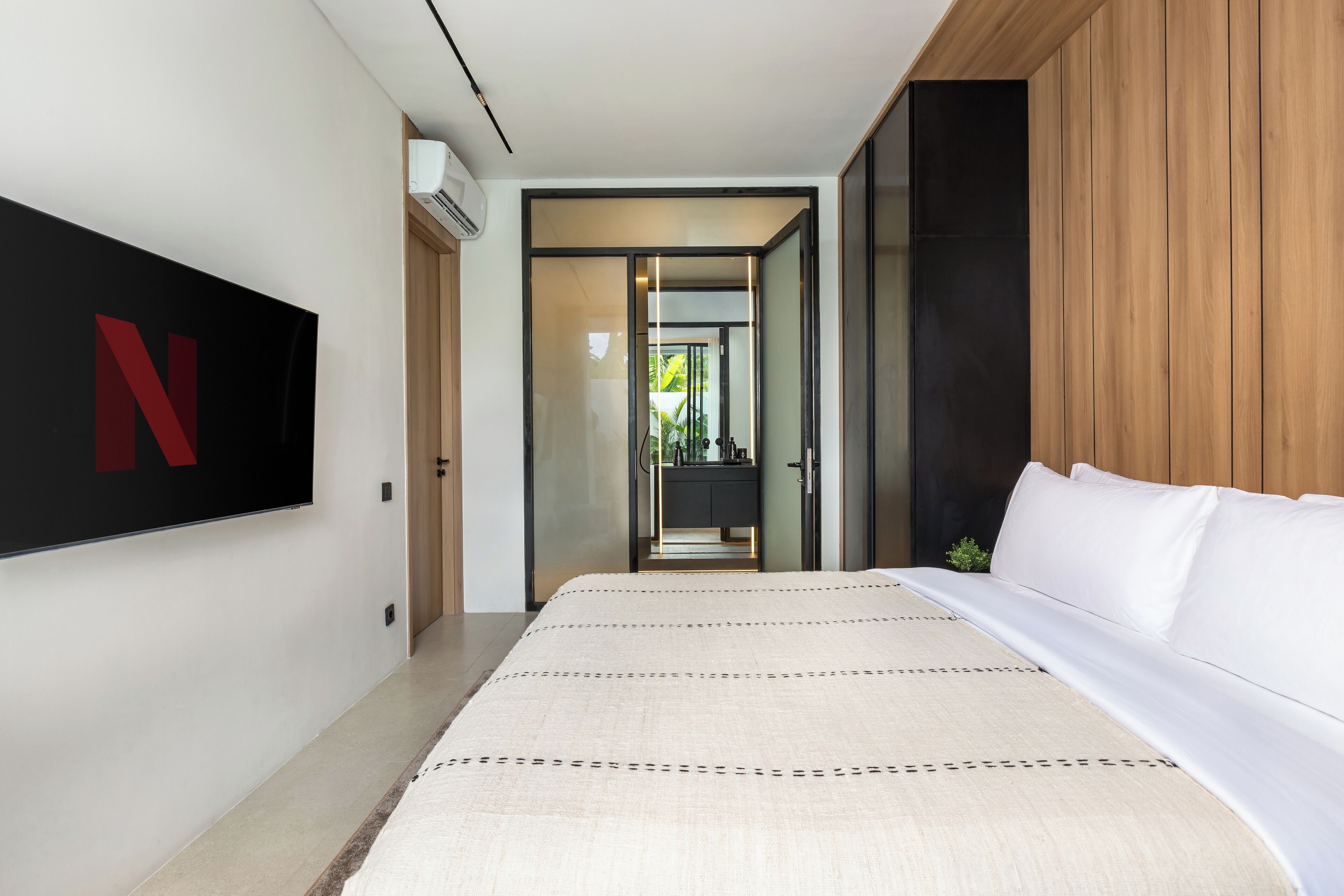 A modern hotel room with a large bed, a flat-screen TV mounted on the wall, and a wooden accent wall.