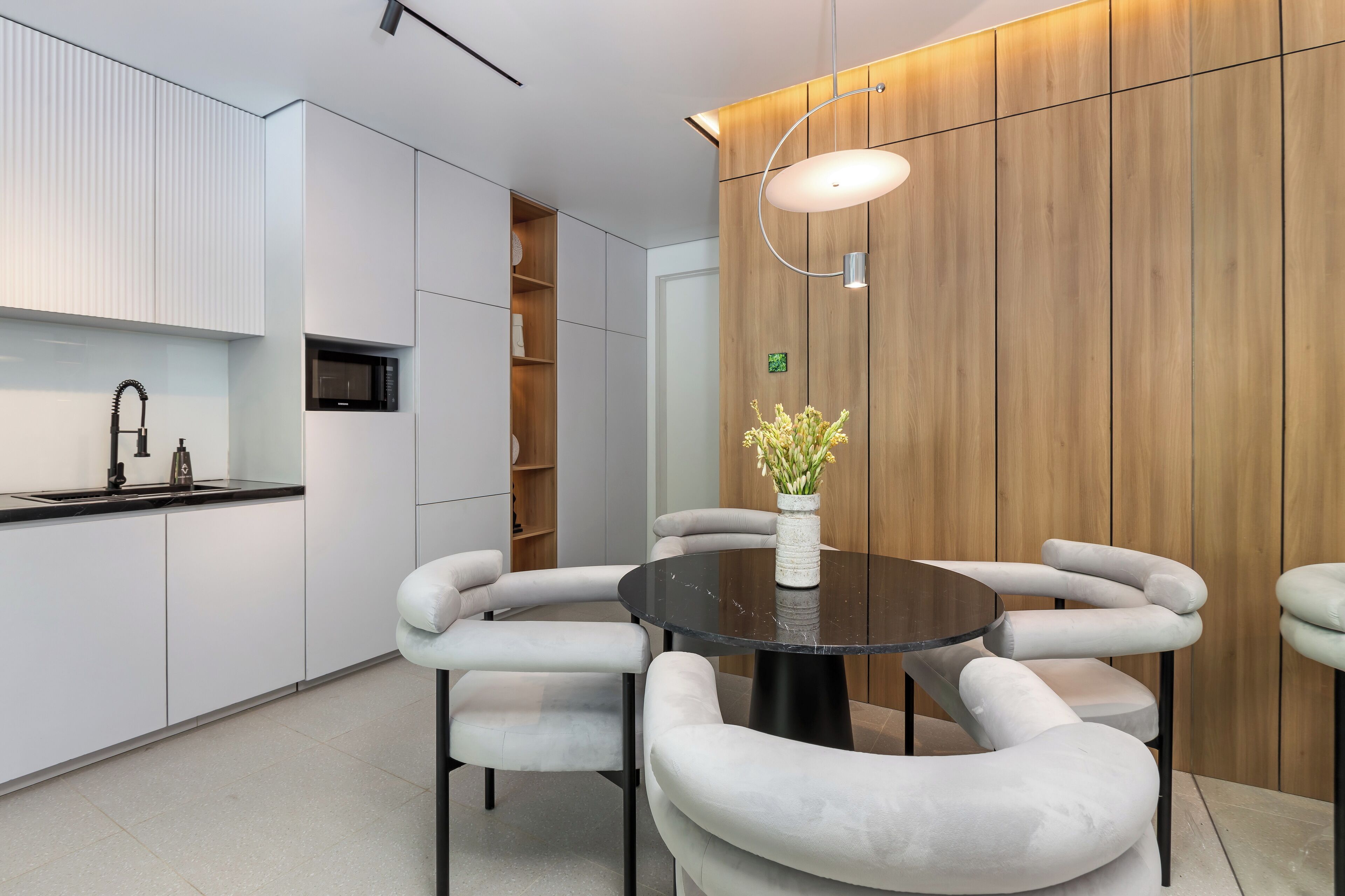 Una cocina moderna con armarios blancos, encimera negra y una mesa redonda con seis sillas.
