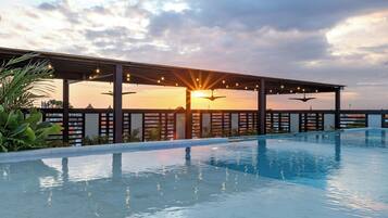 Una piscina con zona cubierta y un atardecer de fondo.