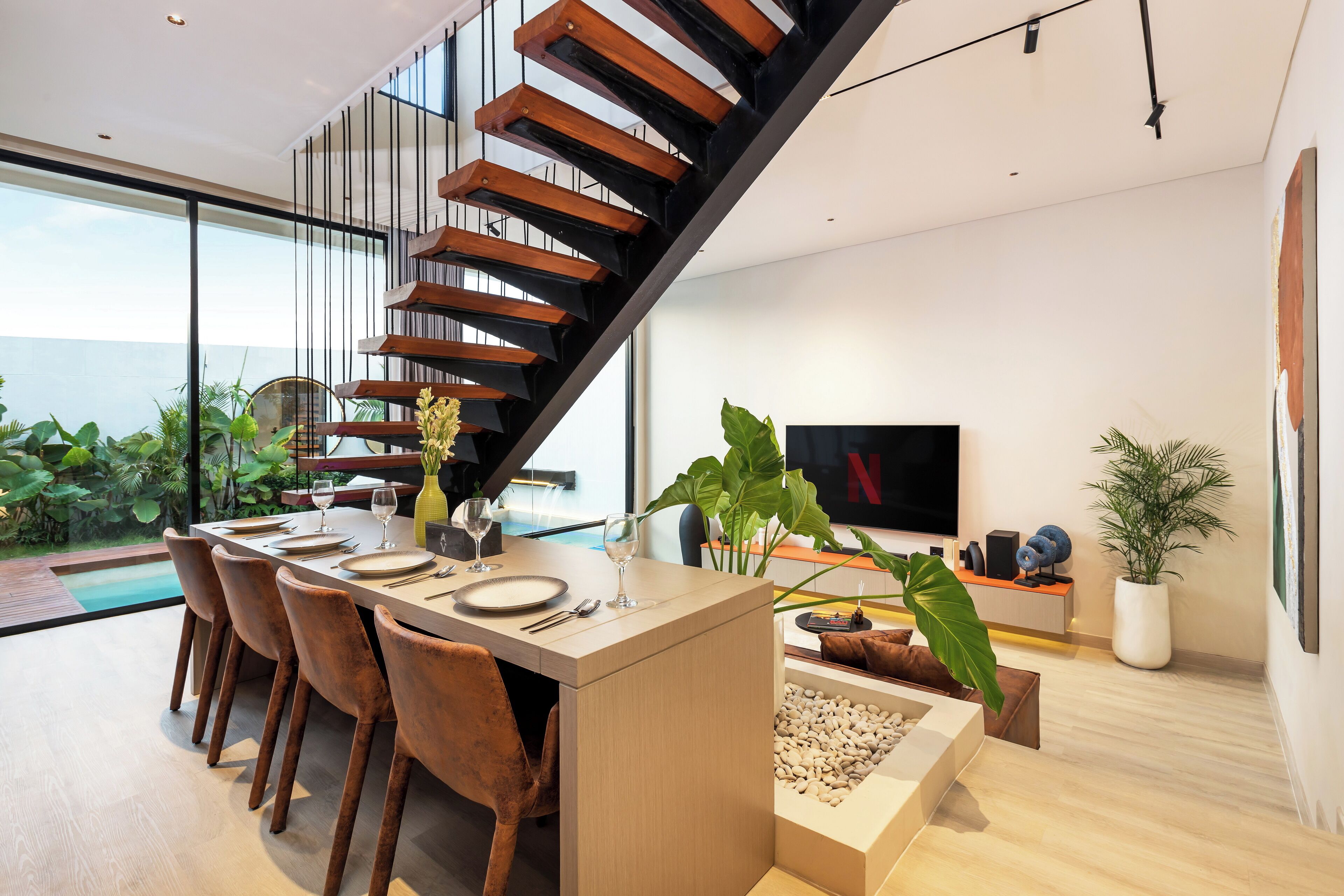 A modern dining area with a wooden staircase, a dining table set for two, and a large potted plant.