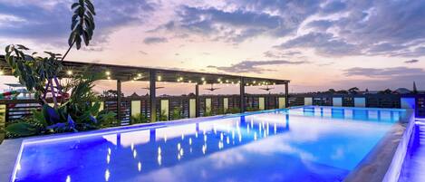 A swimming pool with a pergola and string lights, surrounded by greenery.