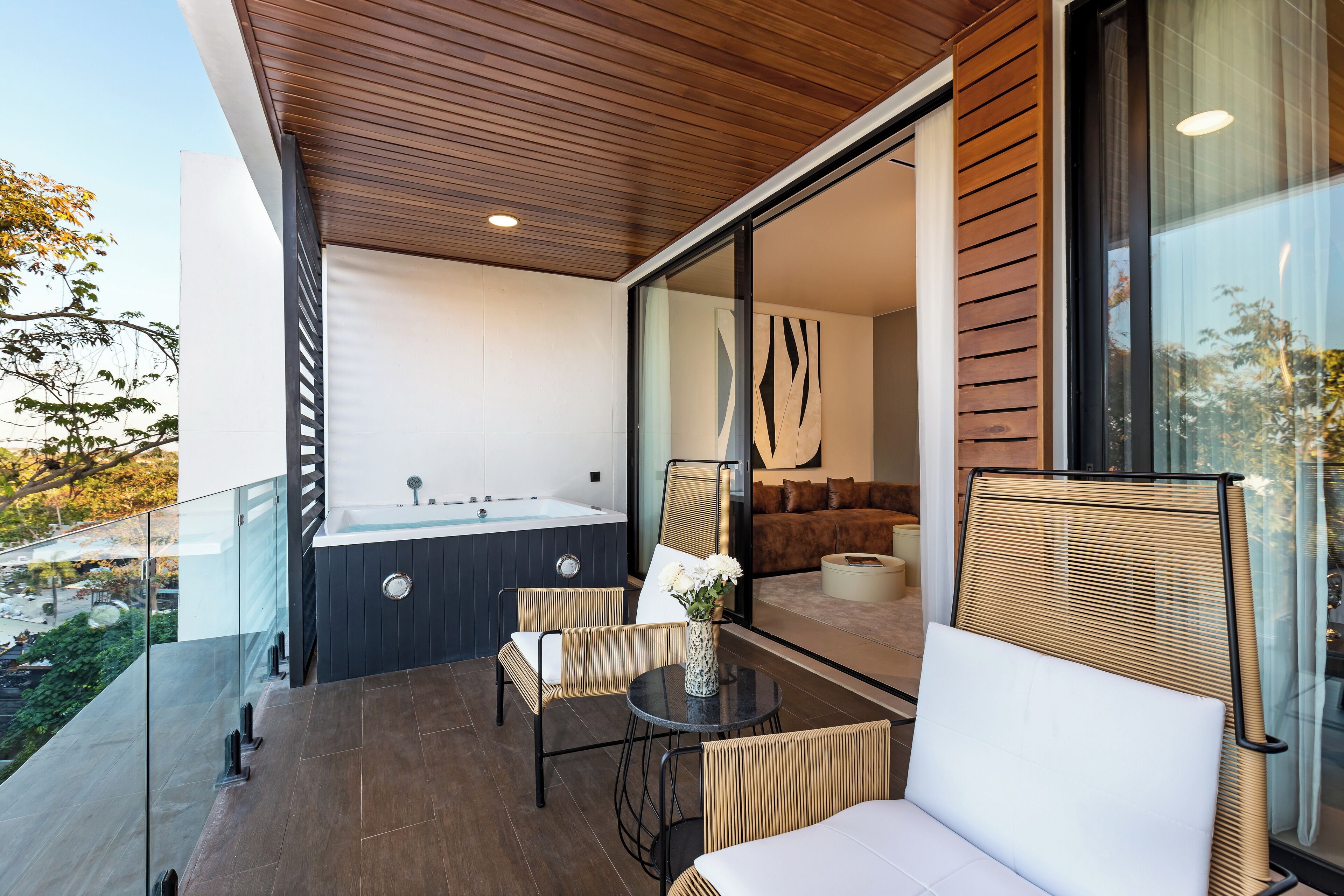Uma varanda moderna ao ar livre com guarda-corpo de vidro, teto de madeira e vista para uma área de spa com hidromassagem e assentos.